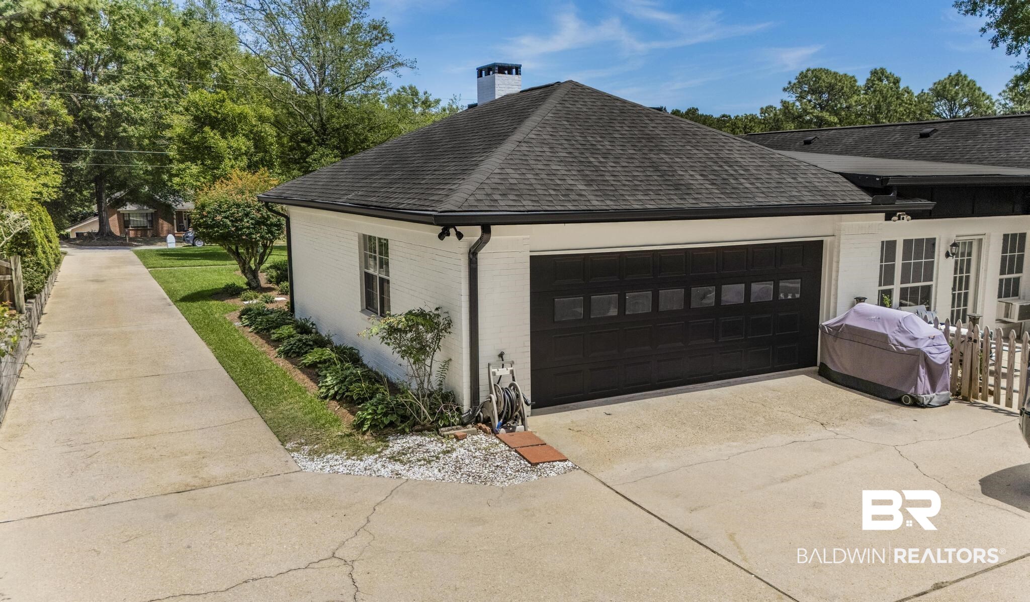 83 Caisson Trace Daphne, AL 36527 - Photo 55 of 63 White brick exterior featuring a black garage door with window inserts, a dark shingle roof, and a concrete driveway