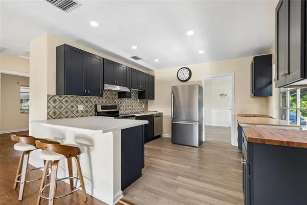 a kitchen with stainless steel appliances granite countertop a refrigerator a stove a sink cabinets and a wooden floor