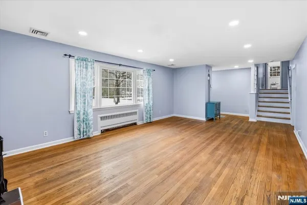 a view of an empty room with wooden floor and a kitchen