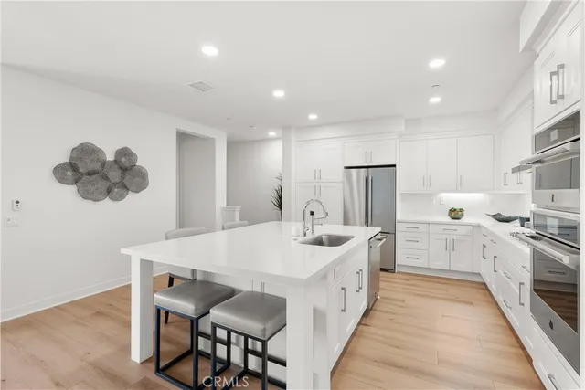 a large white kitchen with a stove a sink a kitchen island with chairs and wooden floor