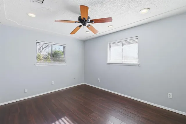 an empty room with wooden floor fan and windows