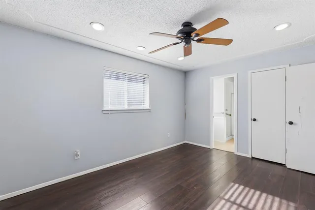 a view of an empty room with wooden floor and a ceiling fan