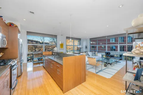 a living room with furniture a rug kitchen view and large windows