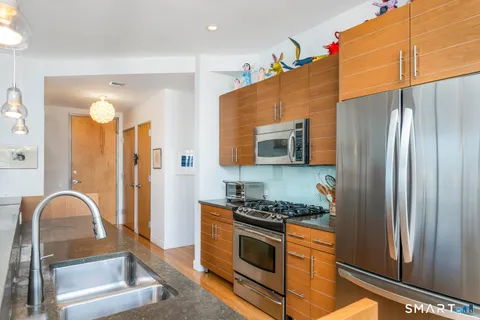 a kitchen with stainless steel appliances granite countertop a refrigerator a stove and a sink with wooden floor