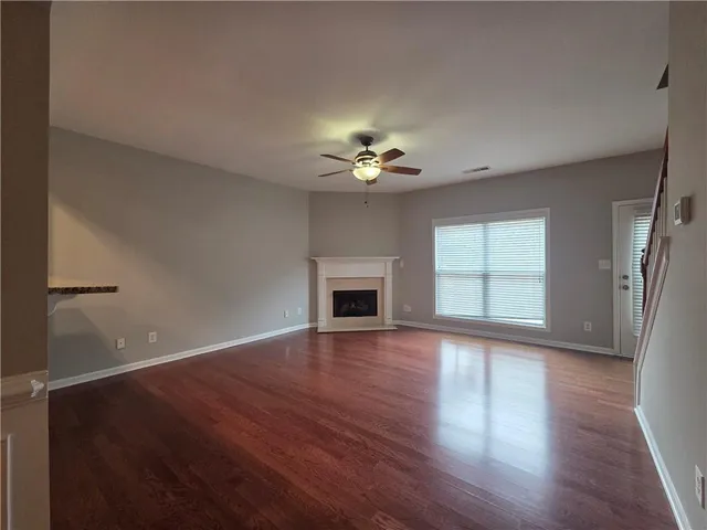 a view of an empty room with wooden floor and a ceiling fan