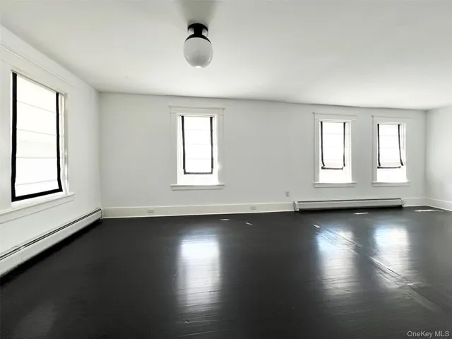 an empty room with wooden floor and windows with curtains