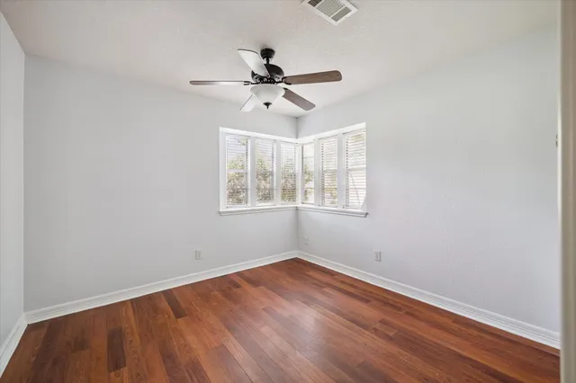 an empty room with wooden floor ceiling fan and windows