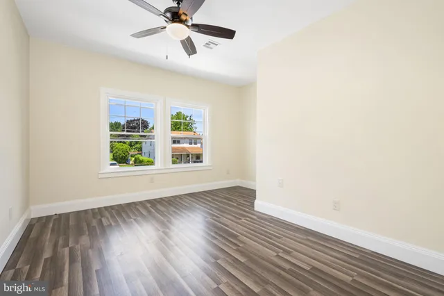 an empty room with wooden floor chandelier fan and windows