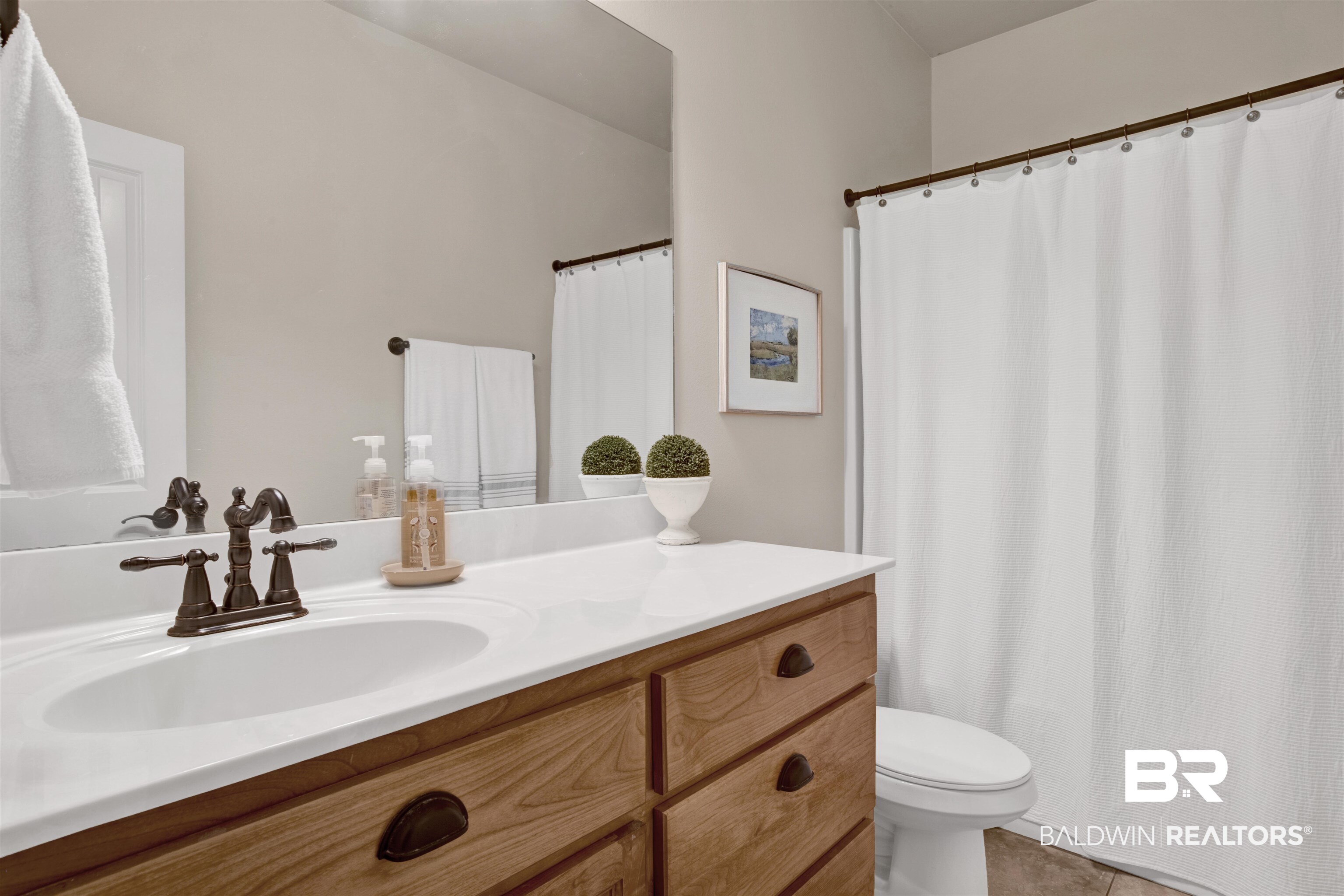 10368 Gayfer Rd Extension Fairhope, AL 36532 - Photo 27 of 43 Bathroom vanity featuring a white countertop with integrated sink, bronze-finish faucet, and wood-finish cabinetry with dark hardware