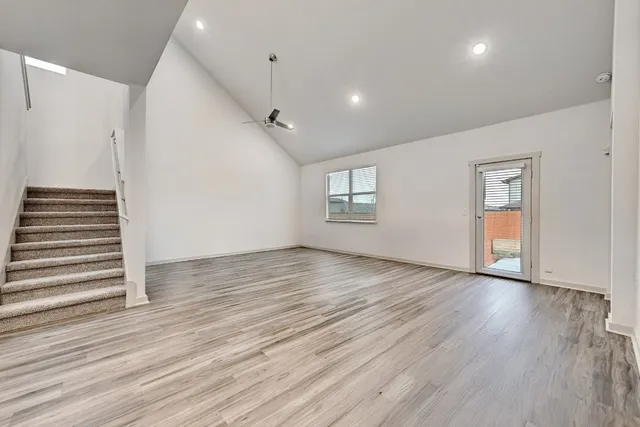 an empty room with wooden floor kitchen view and windows