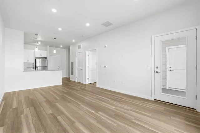 a view of empty room with wooden floor and kitchen