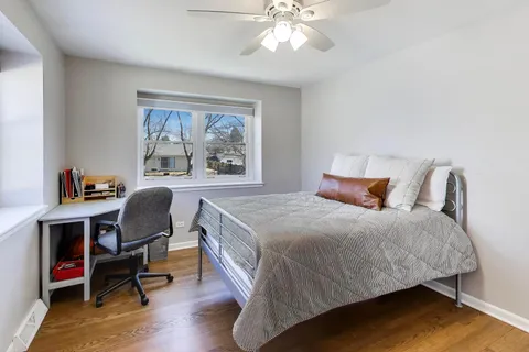 a bedroom with a bed a desk and chair with wooden floor