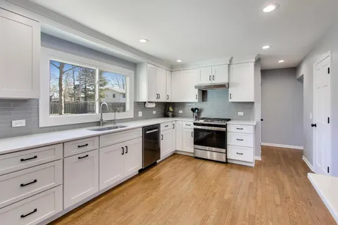 a kitchen with granite countertop a stove top oven a sink dishwasher and white cabinets with wooden floor