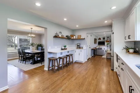 a open kitchen with stainless steel appliances granite countertop a dining table chairs stove refrigerator and cabinets