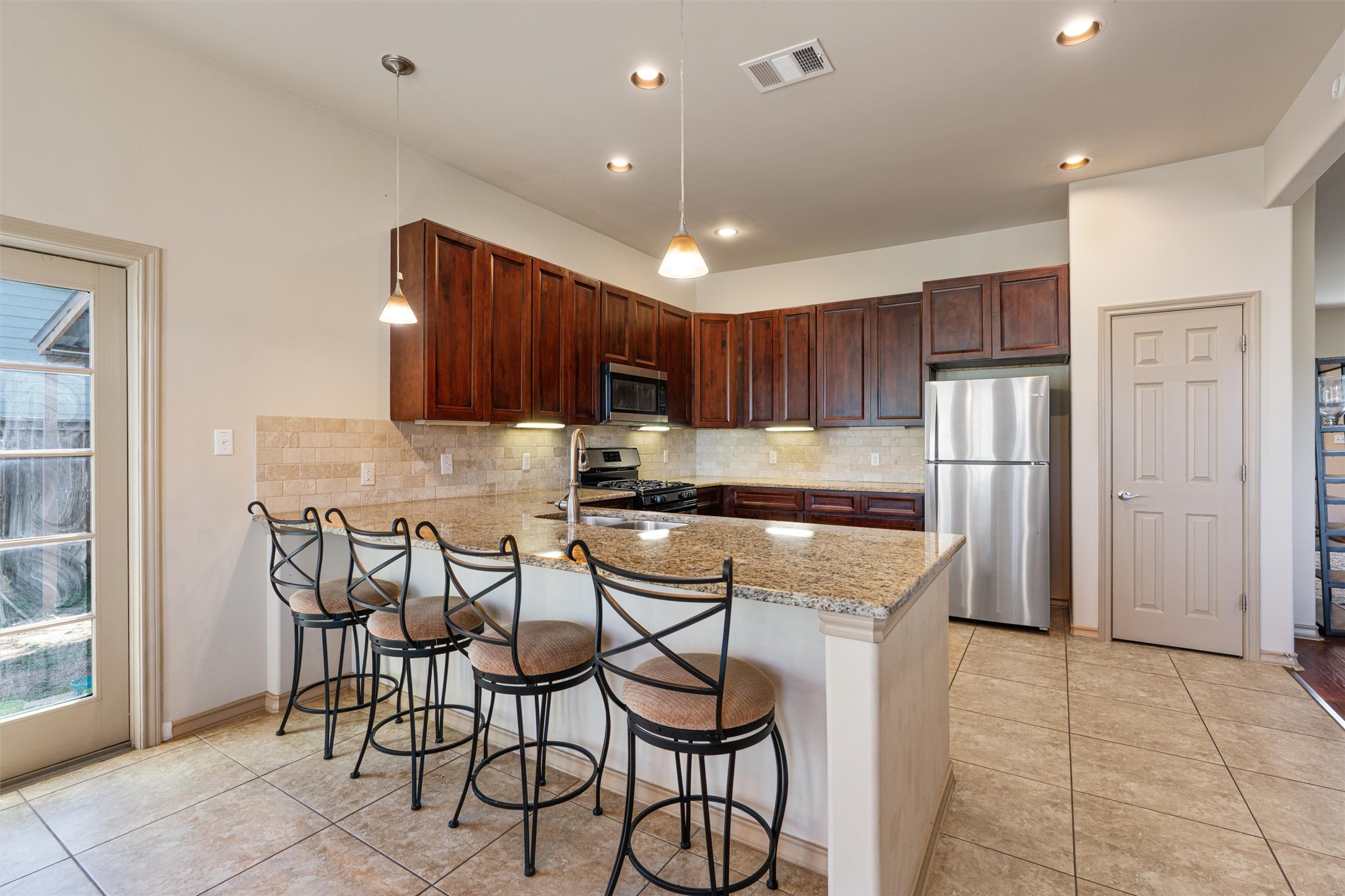 209 Harris Street Elgin, TX 78621 - Photo 10 of 40 Kitchen featuring a peninsula, stainless steel appliances, light stone countertops, pendant lighting, and a kitchen breakfast bar
