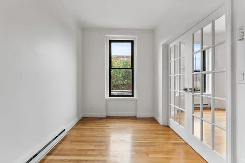 a view of an empty room with wooden floor and a window