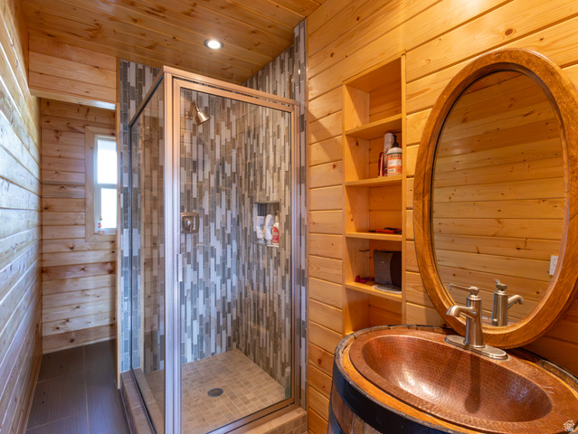 4770 Pine Crest Road Evanston, UT 82930 - Photo 14 of 24 Bathroom featuring wood-finish walls and ceiling, a glass-enclosed shower with mosaic tile surround, a recessed shower niche, an oval-framed mirror, and a copper vessel sink set within a barrel-style vanity