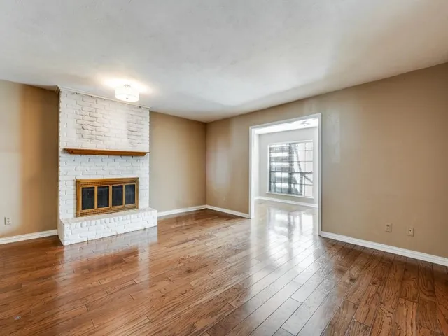 a view of an empty room with wooden floor and a fireplace