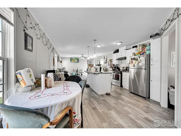 a open kitchen with stainless steel appliances kitchen island granite countertop a refrigerator a stove a sink dishwasher and white cabinets with wooden floor