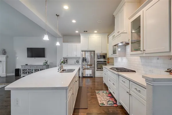 a kitchen with stainless steel appliances a stove top oven a sink a refrigerator and white cabinets