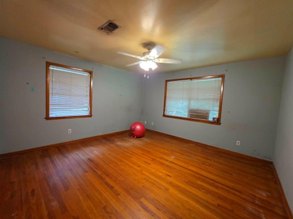 4514 West Loop 281 Longview, TX 75604 - Photo 27 of 36 Spacious room featuring wood-finish flooring, two windows with wood trim, and a ceiling fan with integrated lighting