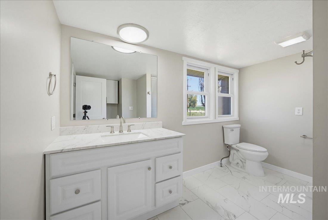 30013 Apple Valley Road Parma, ID 83660 - Photo 15 of 25 Bathroom featuring a white vanity with a light-toned countertop, a large wall-mounted mirror, white rectangular floor tiles, and a window