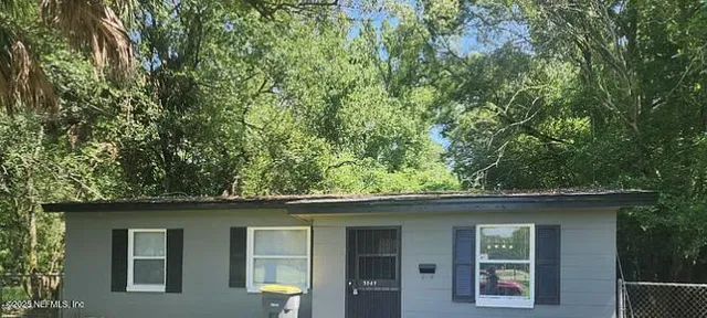 a small barn in front of a house with a large tree