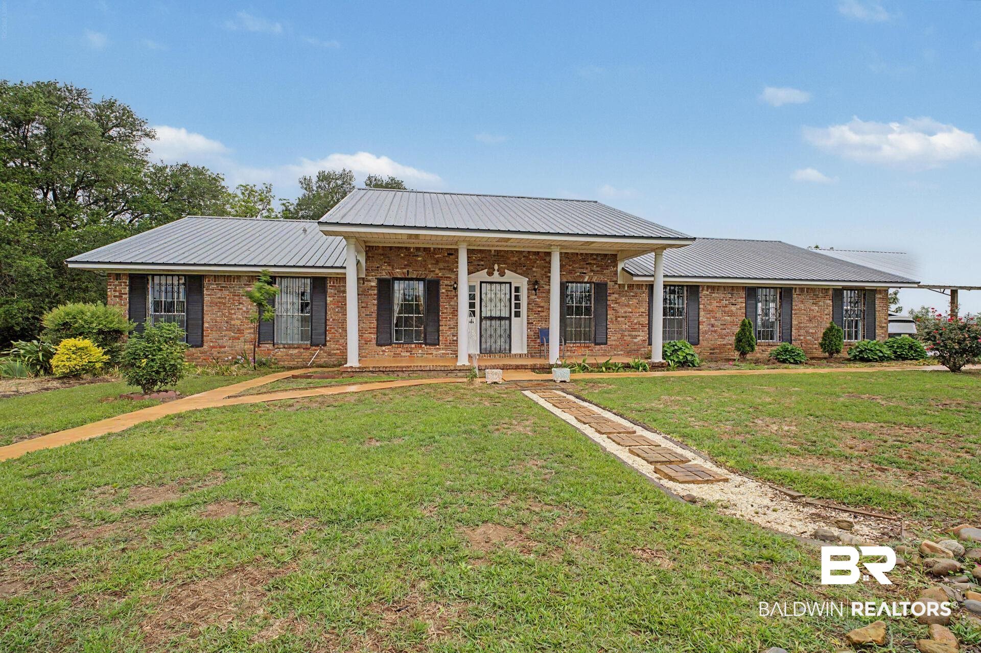 3791 Robinsonville Road Atmore, AL 36502 - Photo 10 of 47 Brick facade residence featuring a covered front porch with white pillars, a gray metal roof, and dark window shutters