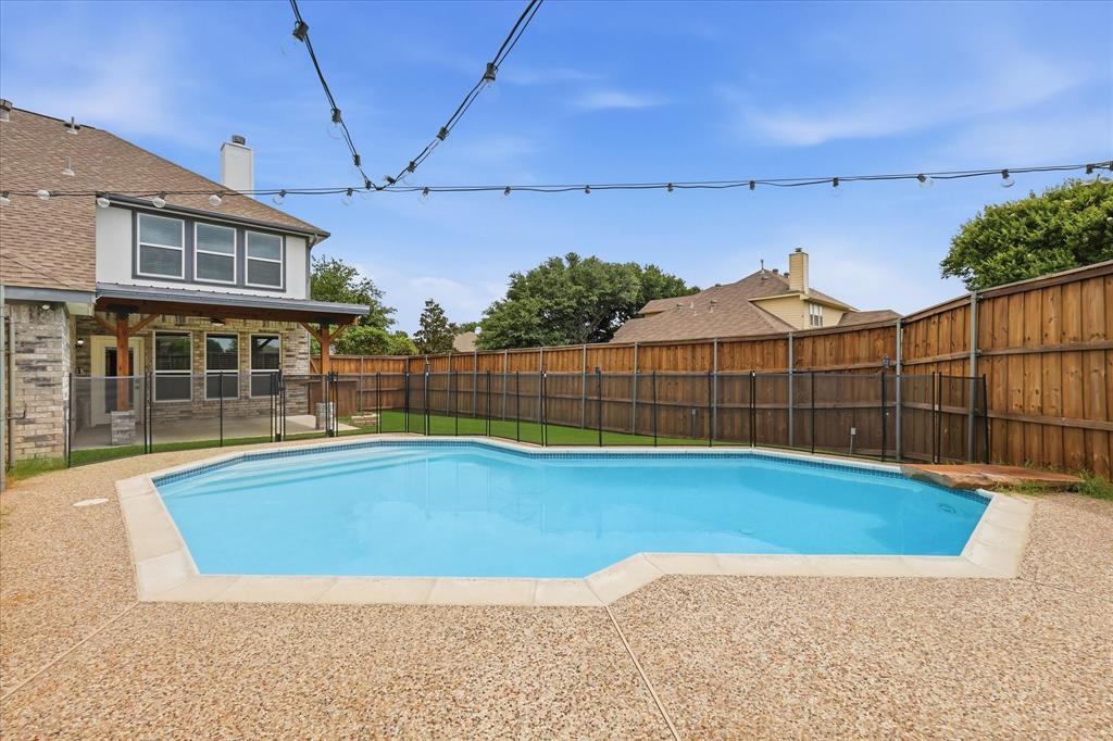 4545 Ridgepointe Drive The Colony, TX 75056 - Photo 13 of 37 Spacious backyard featuring a built-in swimming pool with a black safety fence, surrounding aggregate concrete patio, and a wood privacy fence