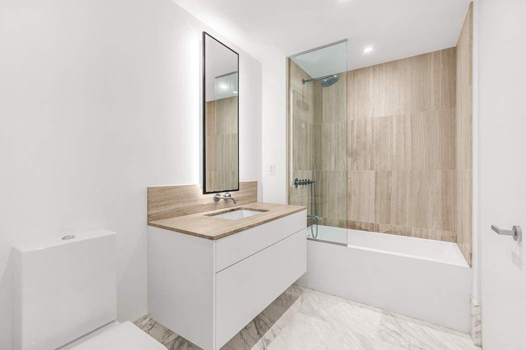 429 Kent Avenue, Unit 503 Brooklyn, NY 11249 - Photo 10 of 14 a bathroom with a granite countertop sink a mirror and a bathtub