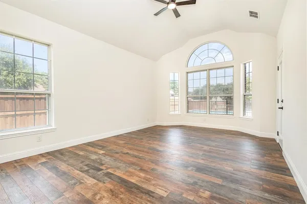 an empty room with wooden floor fan and windows