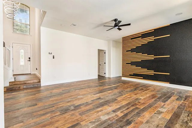 a view of an empty room with wooden floor and a ceiling fan