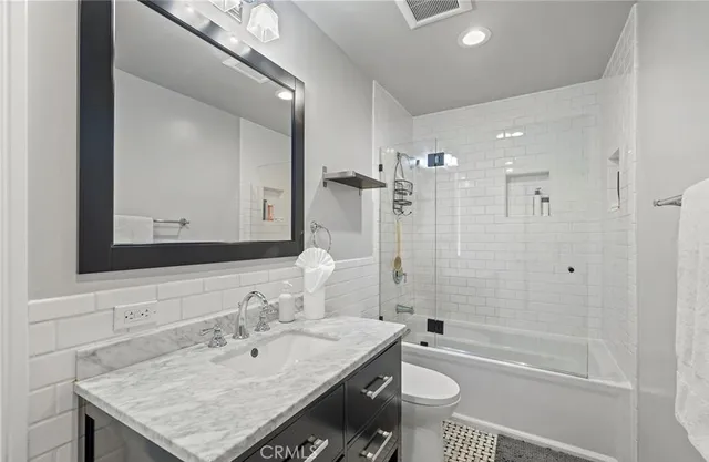 a bathroom with a granite countertop sink a toilet a mirror and shower