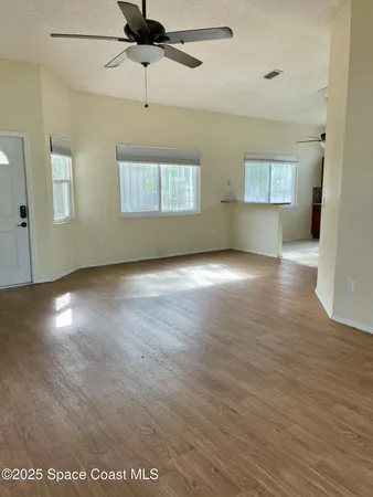 an empty room with wooden floor chandelier and windows