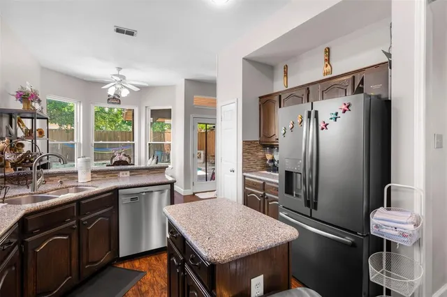 a kitchen with stainless steel appliances granite countertop a refrigerator a sink dishwasher a stove and white countertops with wooden floor