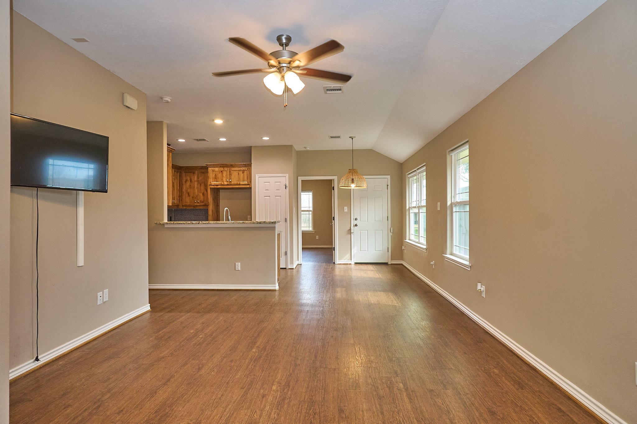 1807 Nuches Lane Bryan, TX 77803 - Photo 5 of 27 This room features an open layout with wood flooring, neutral walls, and a ceiling fan. It includes a kitchen area with wooden cabinets, a breakfast bar, and ample natural light from multiple windows.