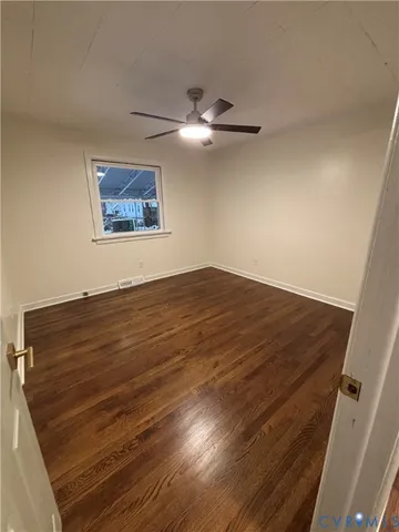 a view of an empty room with wooden floor and a ceiling fan