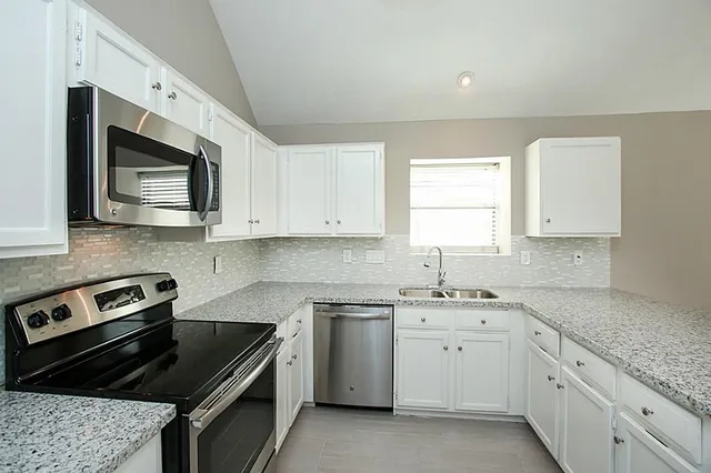 a kitchen with white cabinets a sink stove and microwave