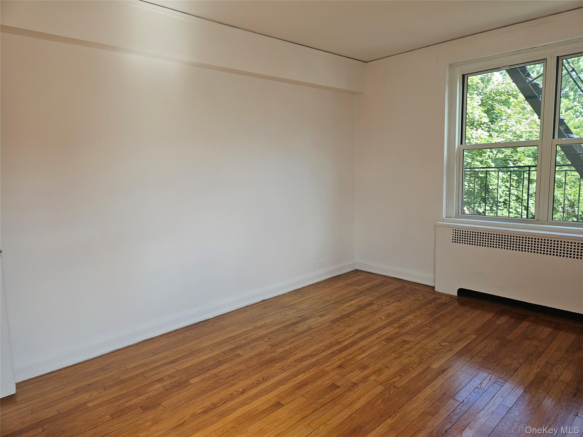 72-15 37th Avenue, Unit 3H Queens, NY 11372 - Photo 11 of 14 Empty room with radiator and light wood-type flooring