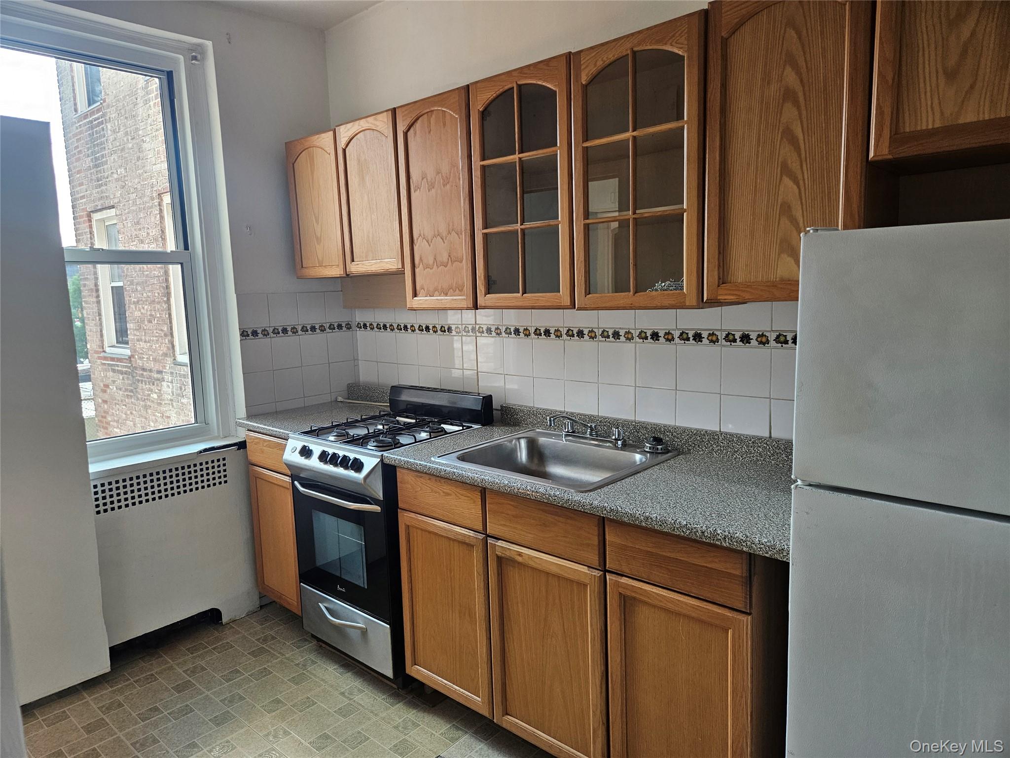 72-15 37th Avenue, Unit 3H Queens, NY 11372 - Photo 13 of 14 Kitchen featuring freestanding refrigerator, stainless steel gas range, radiator, glass insert cabinets, and decorative backsplash