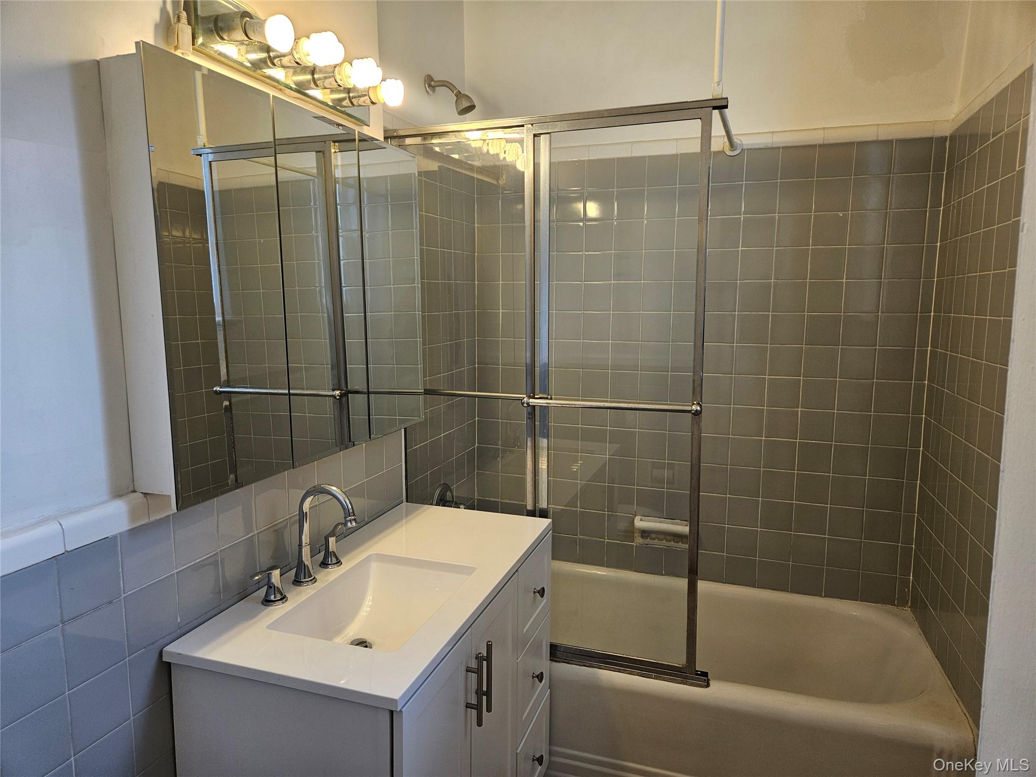72-15 37th Avenue, Unit 3H Queens, NY 11372 - Photo 10 of 14 Bathroom featuring vanity, shower / bath combination with glass door, and tile walls