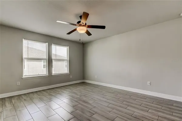 an empty room with wooden floor fan and windows