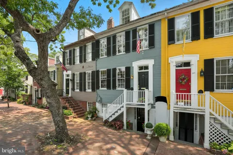 a front view of a building with large trees and plants