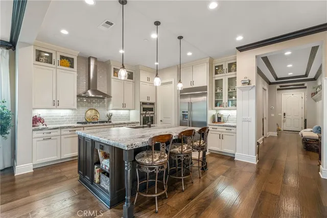 a kitchen with stainless steel appliances granite countertop a stove a refrigerator a kitchen island a dining table and chairs with wooden floor