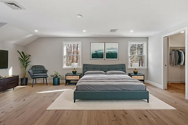 a bedroom with a large bed a potted plant on dresser and a wooden floor