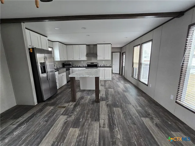 a kitchen with stainless steel appliances a refrigerator a sink dishwasher a stove top oven a wooden floor and a window