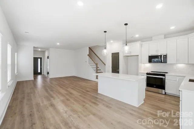 a large white kitchen with stainless steel appliances kitchen island granite countertop a stove a refrigerator a sink and a oven with wooden floor