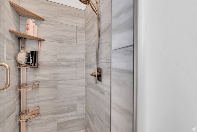 6105 Bunda Way St. George, UT 84790 - Photo 21 of 49 Shower stall featuring large-format tile walls, a rain showerhead, a wall-mounted shower handle, and a glass shower door with a brass handle