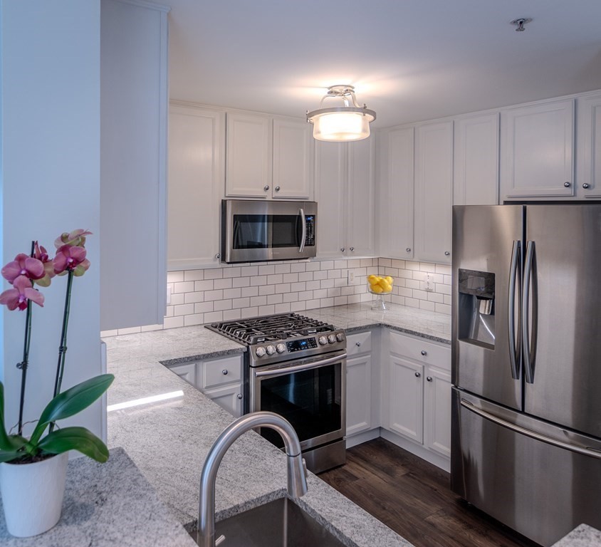 a kitchen with stainless steel appliances granite countertop a refrigerator a sink a stove and white cabinets