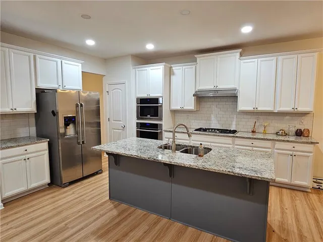 a kitchen with stainless steel appliances granite countertop a refrigerator a sink dishwasher a stove and white countertops with wooden floor